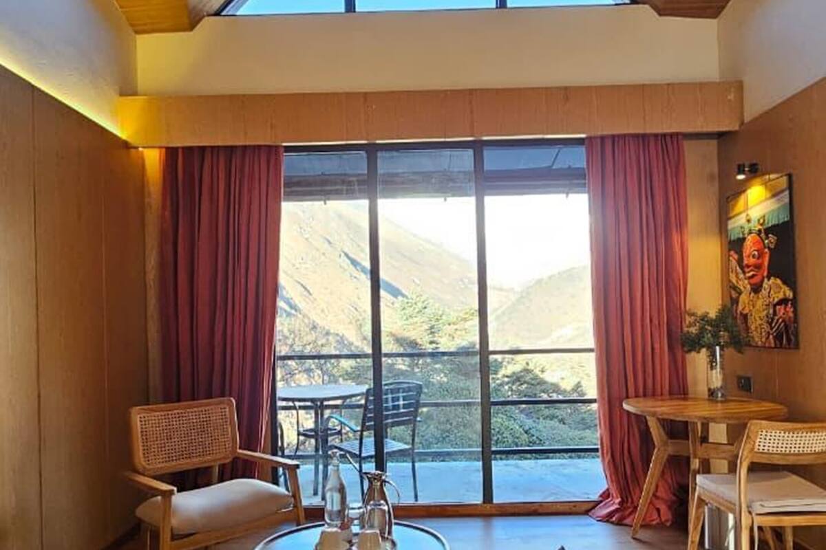 A cozy living room with a high ceiling, wooden walls, and large windows offering a mountain view.