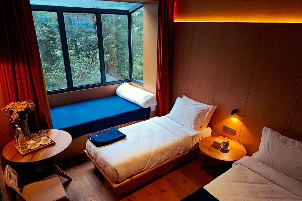 A cozy room with a bed, a small table with a vase of flowers, a chair, and a window with curtains.