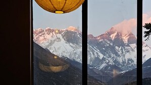 A dining area with a mountain view, tables set with plates and cutlery, and a hanging light fixture. -  The Himalayan Tyangboche (Lukla)
