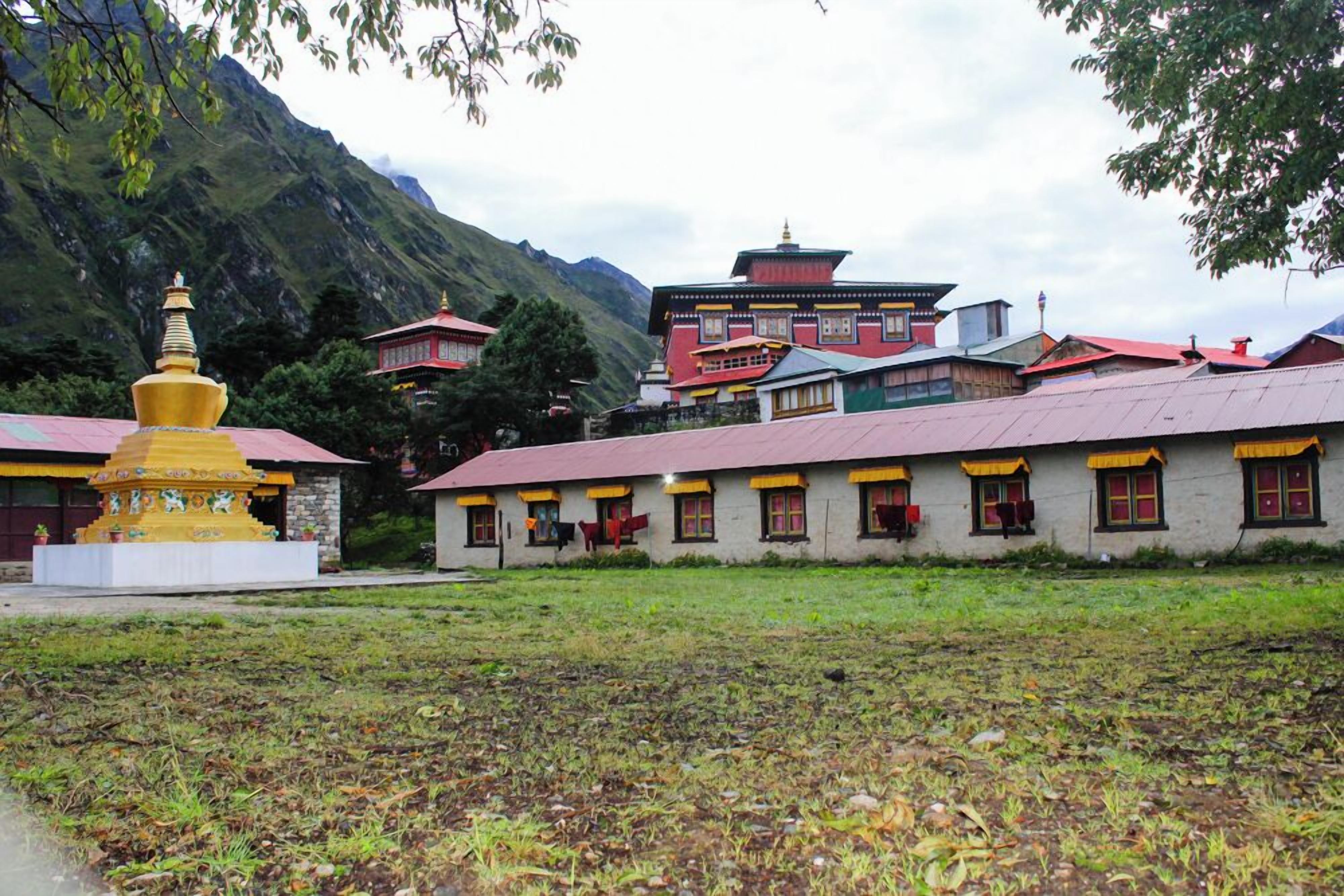 Un bâtiment traditionnel avec un toit rouge et de nombreuses fenêtres, entouré d’une zone herbeuse et avec des montagnes en arrière-plan.