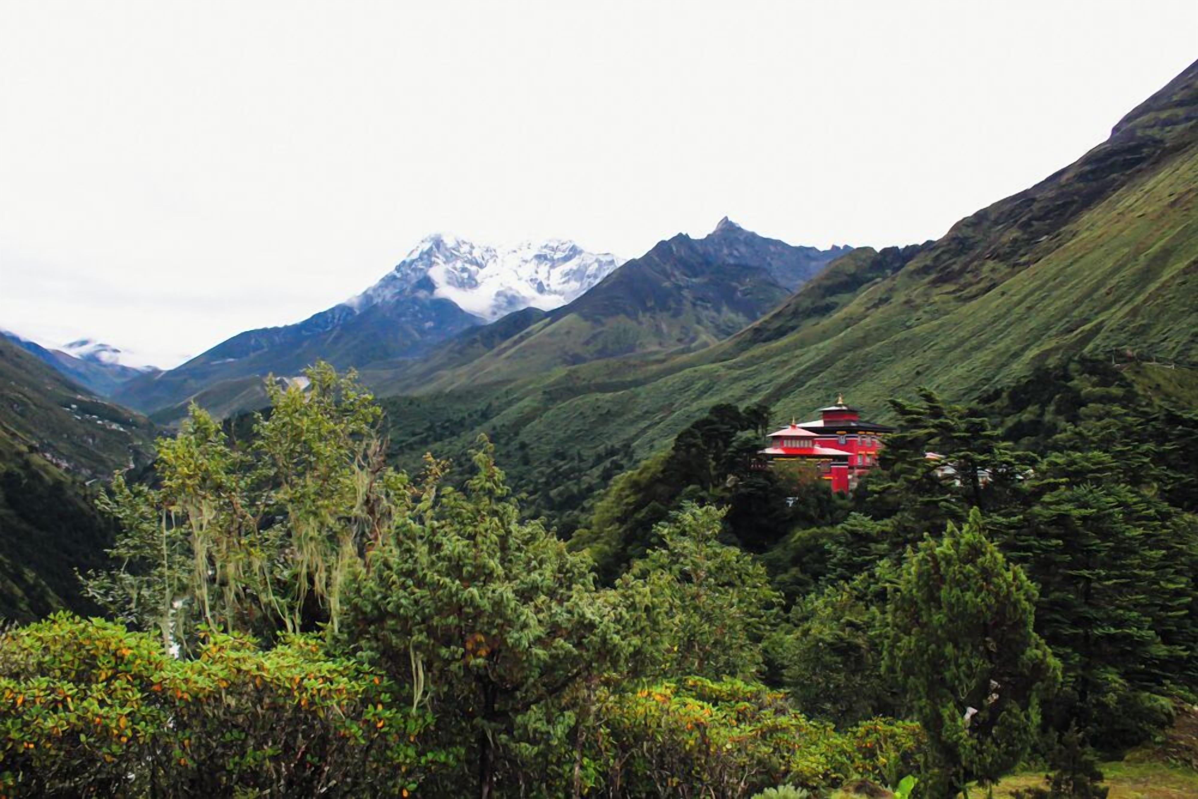 A traditional red building nestled in a lush valley with mountains in the background.