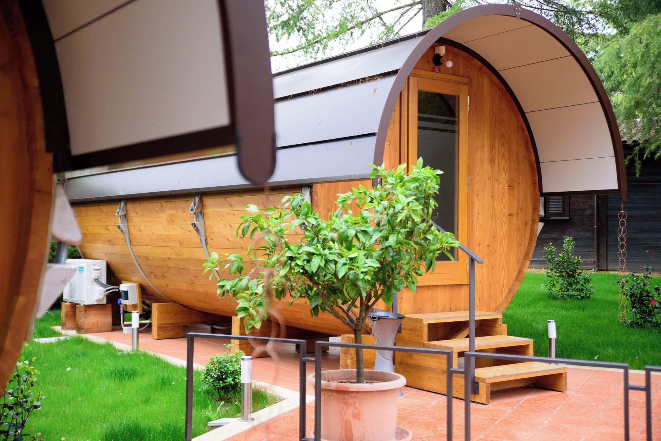 Una estructura de madera con una entrada arqueada, una planta en maceta y un pequeño espacio de estar al aire libre.