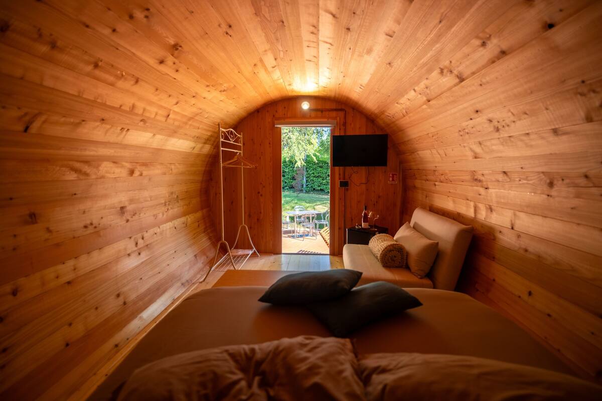 A cozy, wooden cabin bedroom with a bed, pillows, a TV, and a view of the outdoors.