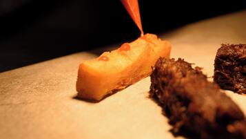 A person using a red piping bag to apply a substance to a food item on a cutting board.