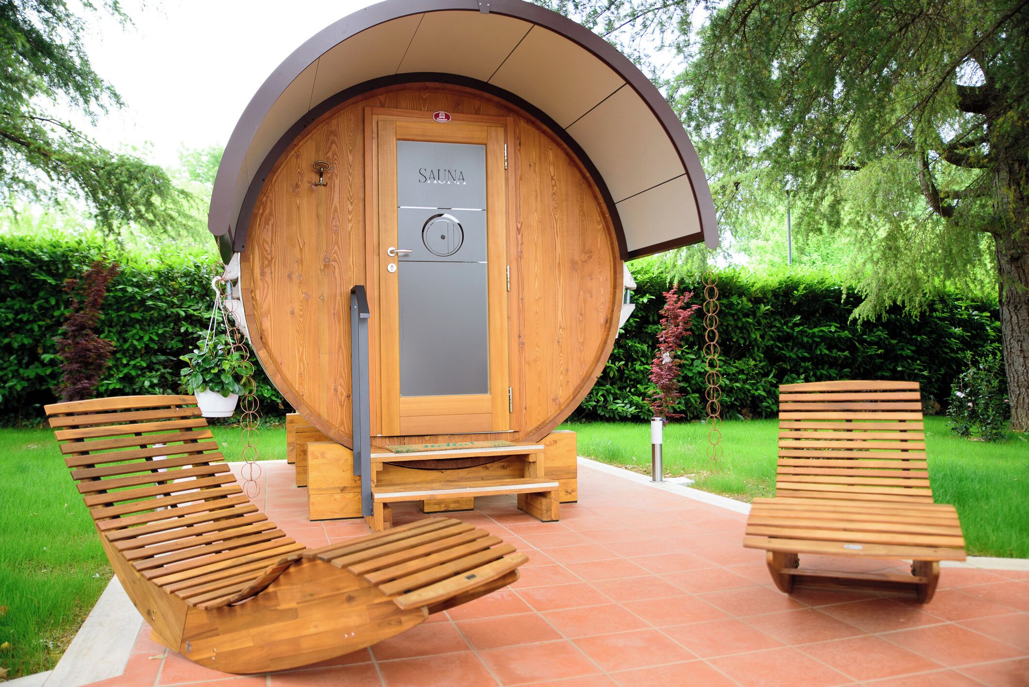 A wooden sauna with a circular door, two wooden loungers, and a small wooden bench.