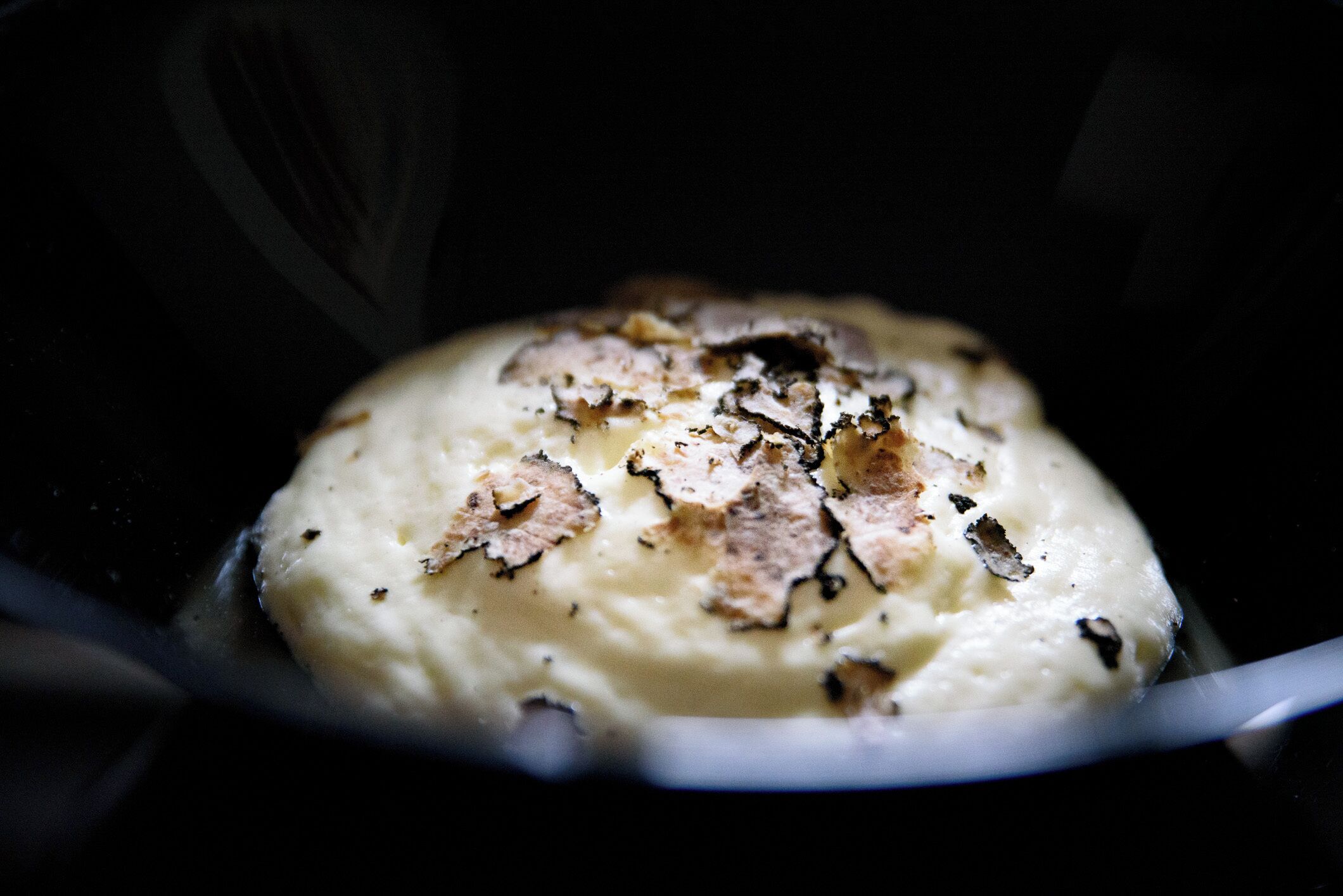 A close-up of a creamy dessert with a caramelized top, possibly a crème brûlée, in a dark bowl.
