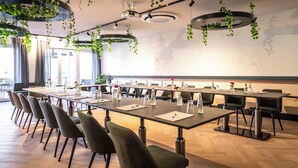 Un salón de conferencias con largas mesas, sillas y plantas colgantes.