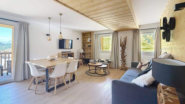 Ett rymligt vardagsrum med ett träpanelat tak, ett matbord med stolar, en soffa och en tv som är monterad på väggen.