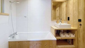 Ett badrum i en stuga med träpanel, ett vitt badkar, en dusch och ett handfat med en spegel ovanför.