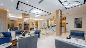 Eine moderne Hotelhalle mit Sitzbereichen, einem Empfangstresen und einer Küche im Hintergrund.