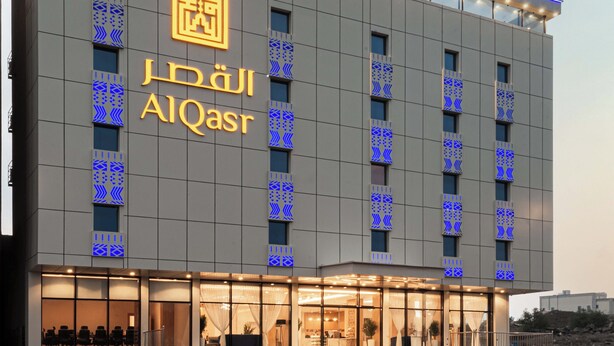 Ein modernes Hotel mit einem auffälligen Wappen-Logo und dem Schriftzug 'AIQasr' an der Fassade.