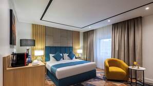 Ein Hotelzimmer mit einem großen Bett, einem Schreibtisch mit Kaffeemaschine, einem Sessel und einem kleinen Tisch mit einem Getränk.