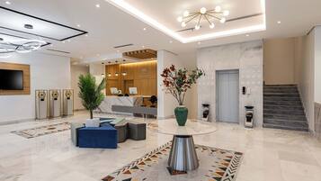 A modern hotel lobby with a reception desk, seating area, and a staircase.
