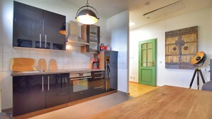 A modern kitchen with dark cabinets, a wooden countertop, and a large island. There is a coffee machine, a hanging light fixture, and a green door in the background. - Vacation apartment "Schwalbennest (Naumburg (Saale))