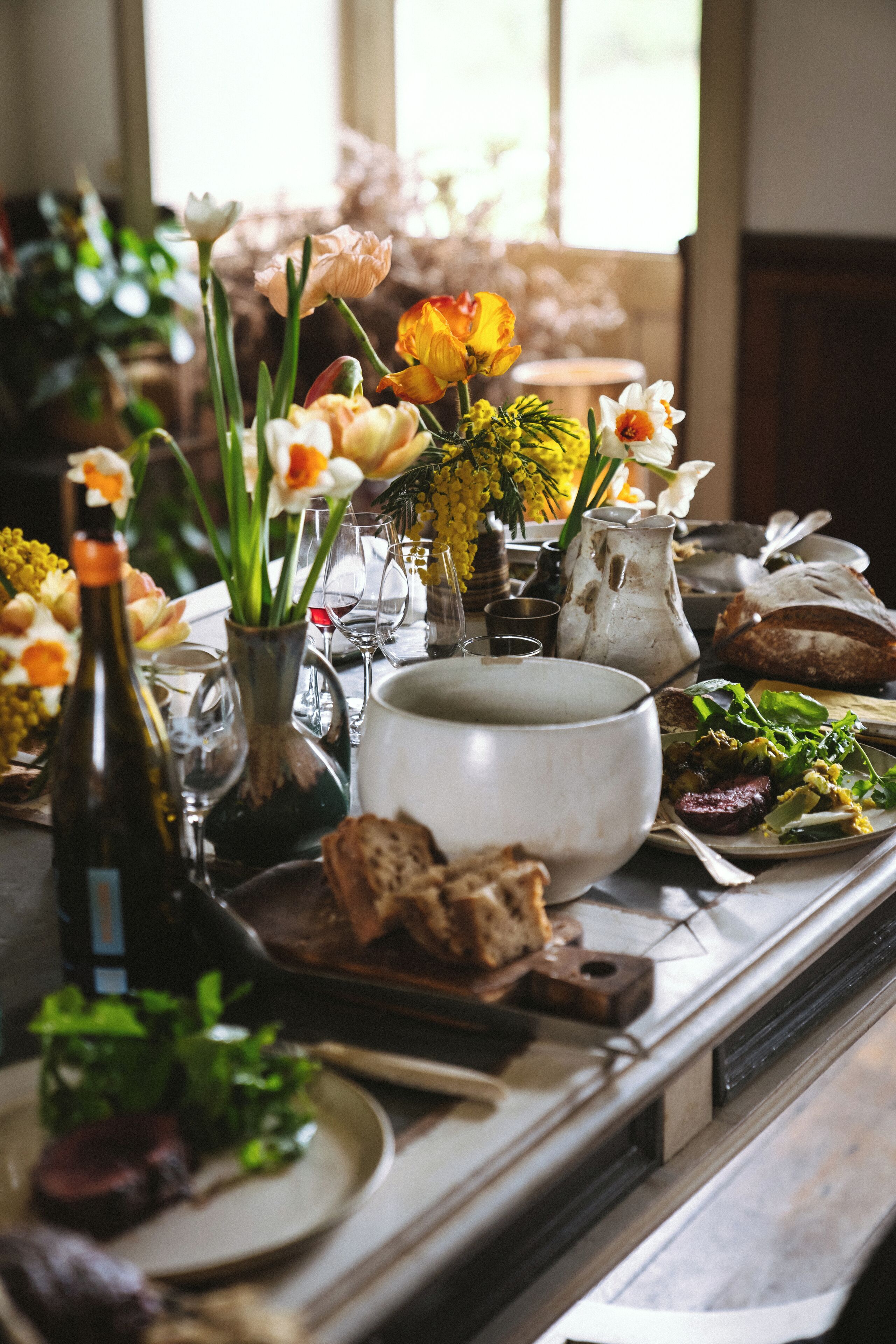 A dining table with various dishes, a vase with flowers, and a bottle of wine.