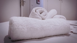 Ein ordentlich gefaltetes weißes Handtuch auf einem Bett in einem Hotelzimmer.