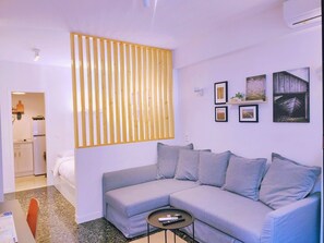 Un soggiorno moderno con un divano grigio, un tavolino e una parete divisoria in listelli di legno. Si vedono quadri appesi alla parete e, sullo sfondo, un angolo cucina.