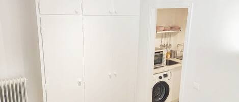 A compact room with a white wardrobe, a washing machine, and a small kitchenette.