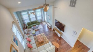 A spacious living room with a large sofa, a television, and a ceiling fan. - Coastal Club Villa: Resort Amenities 3 BR, 2.5 BA (Lewes)