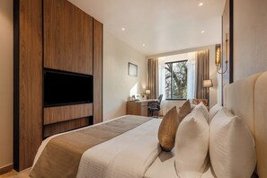 Una habitación de hotel moderna con una cama grande, un escritorio, un televisor de pantalla plana y un ventanal con cortinas.