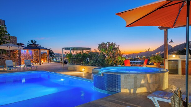 Una piscina con sillas de descanso y un jacuzzi, rodeada por un área de patio con sombrillas y plantas en macetas.