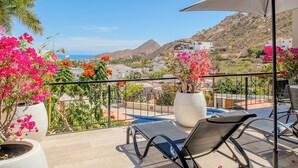 Un balcón con vistas a un paisaje montañoso, una piscina y plantas en macetas.
