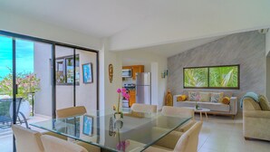 Un espacio habitable moderno con una mesa de comedor de vidrio, sofás beige y una cocina visible a través de una puerta abierta.