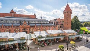 Un bâtiment historique doté d’une tour horlogée, de stands de marché couverts et d’une vaste serre en verre.