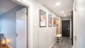 Un couloir avec des œuvres d’art encadrées accrochées au mur, un banc et une porte au fond.