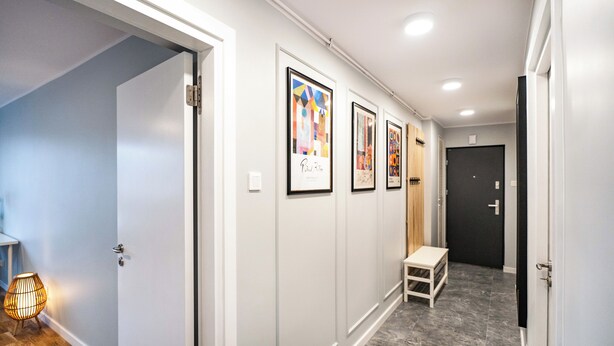 Un couloir avec des œuvres d’art encadrées accrochées au mur, un banc et une porte au fond.