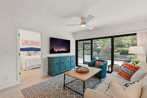 A modern living room with a sofa, a coffee table, a blue armchair, a cabinet, and a bed in the background. - C-122 - Luxury Condo - Easy Walk to Amenities! (Naples)