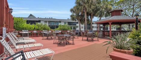 An outdoor patio with multiple barbecue grills, lounge chairs, and tables.