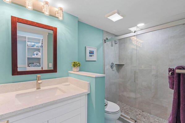 A bathroom with a white sink, a mirror with a wooden frame, a toilet, and a glass-enclosed shower.