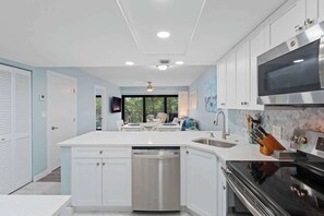 A modern kitchen with white cabinetry, a stainless steel dishwasher, a black stove, and a large window providing a view of the outdoors. - J-357 - Luxury With Private Lanai View & Sleeps 6 (Naples)