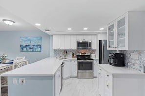 A modern kitchen with white cabinetry, stainless steel appliances, and a marble backsplash.