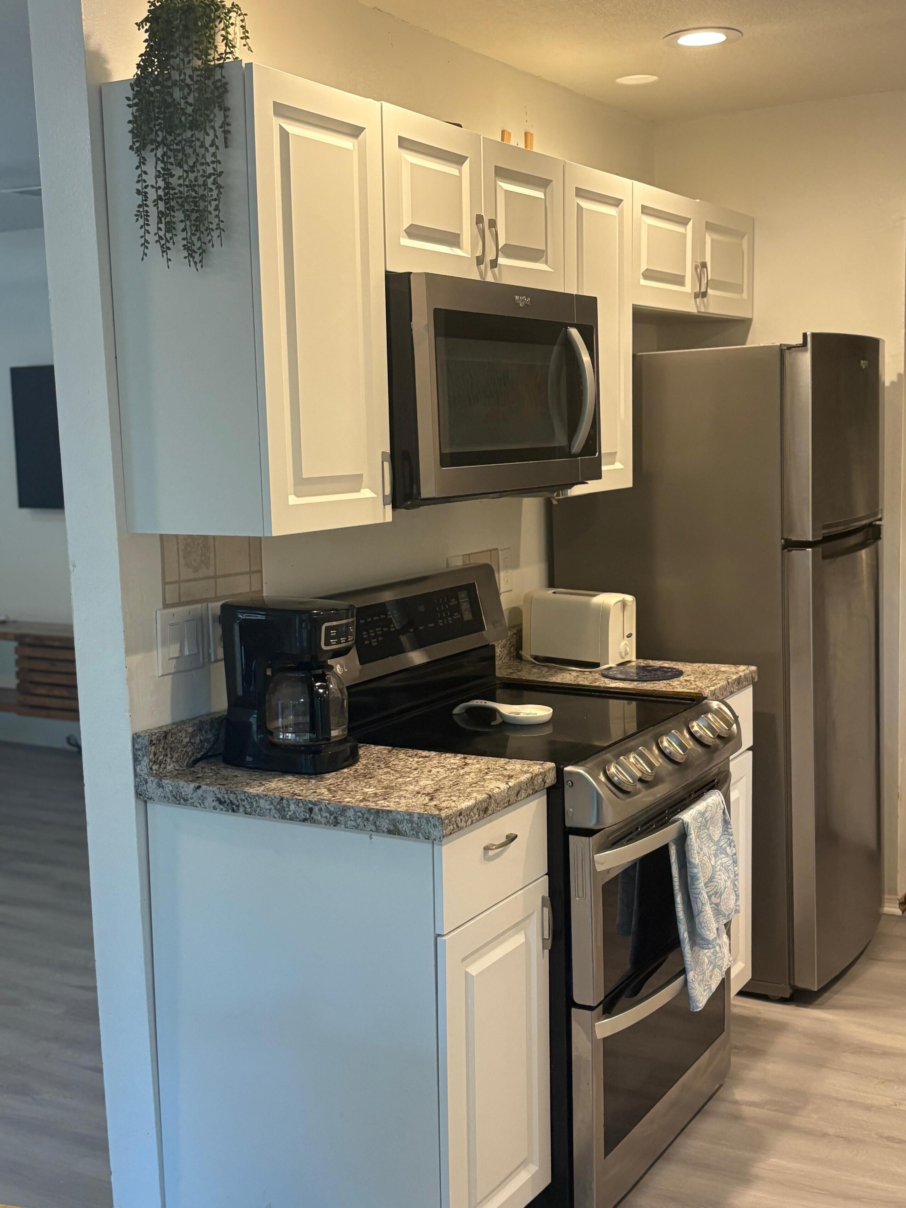 A modern kitchen with white cabinets, a stainless steel refrigerator, a microwave, a coffee maker, and a stove.