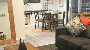 A cozy living room with a sofa, a coffee table, and a dining area with chairs and a table. - Blue Sky StiltsHouse in a Secluded Forest. (Ocala)