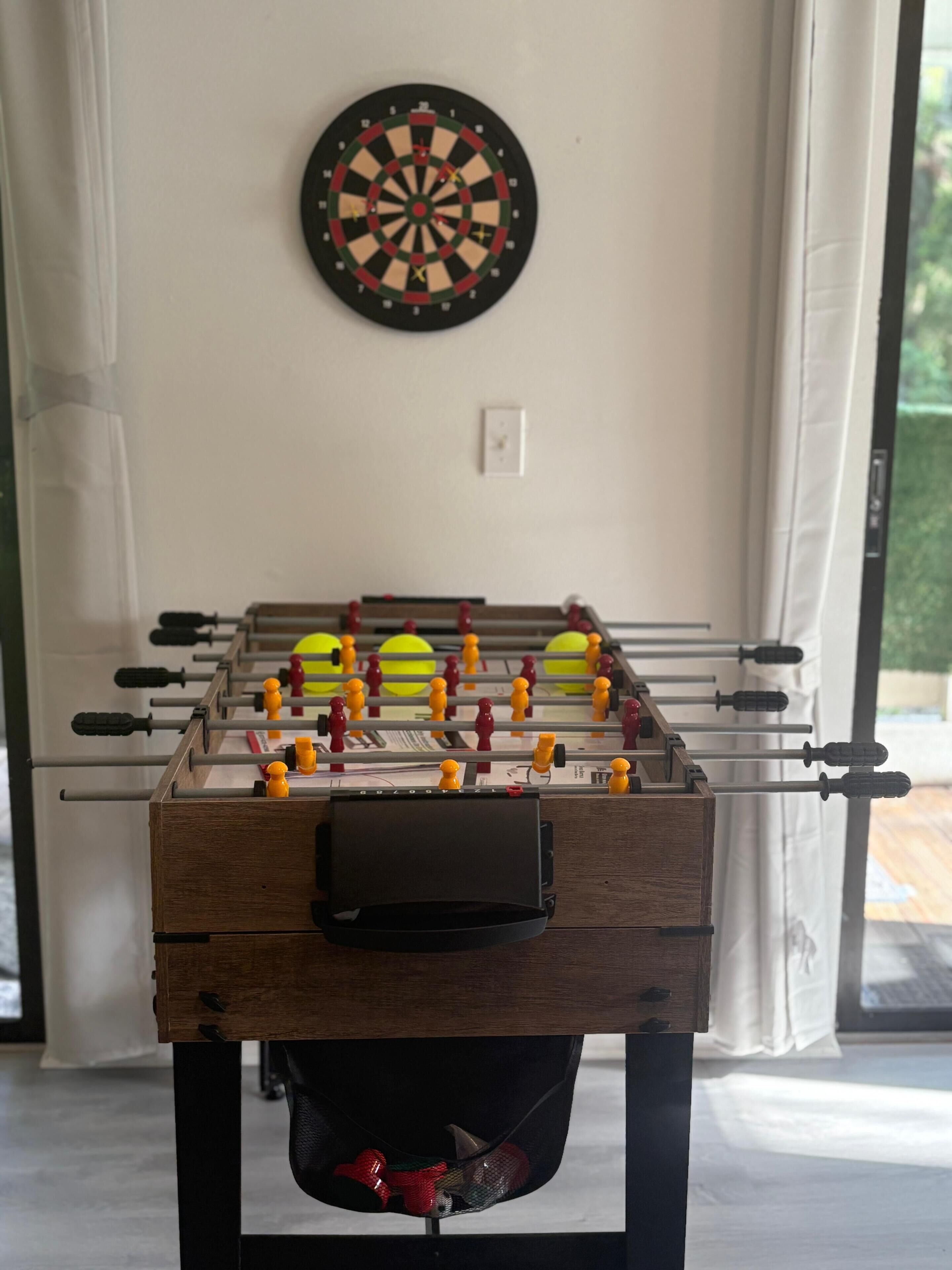A foosball table with a dartboard on the wall.