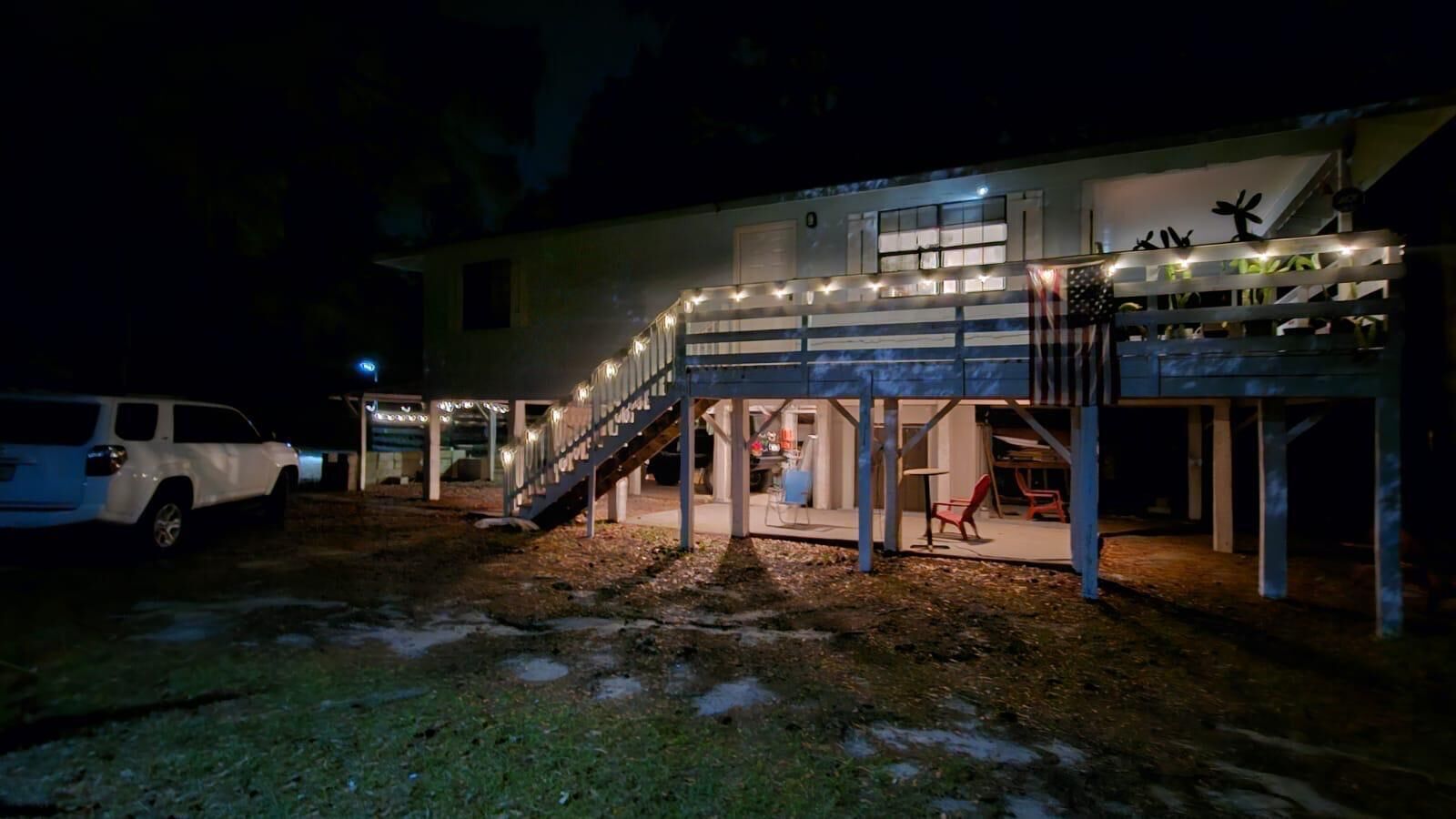A two-story building with a covered outdoor area, a staircase, and a vehicle parked nearby.