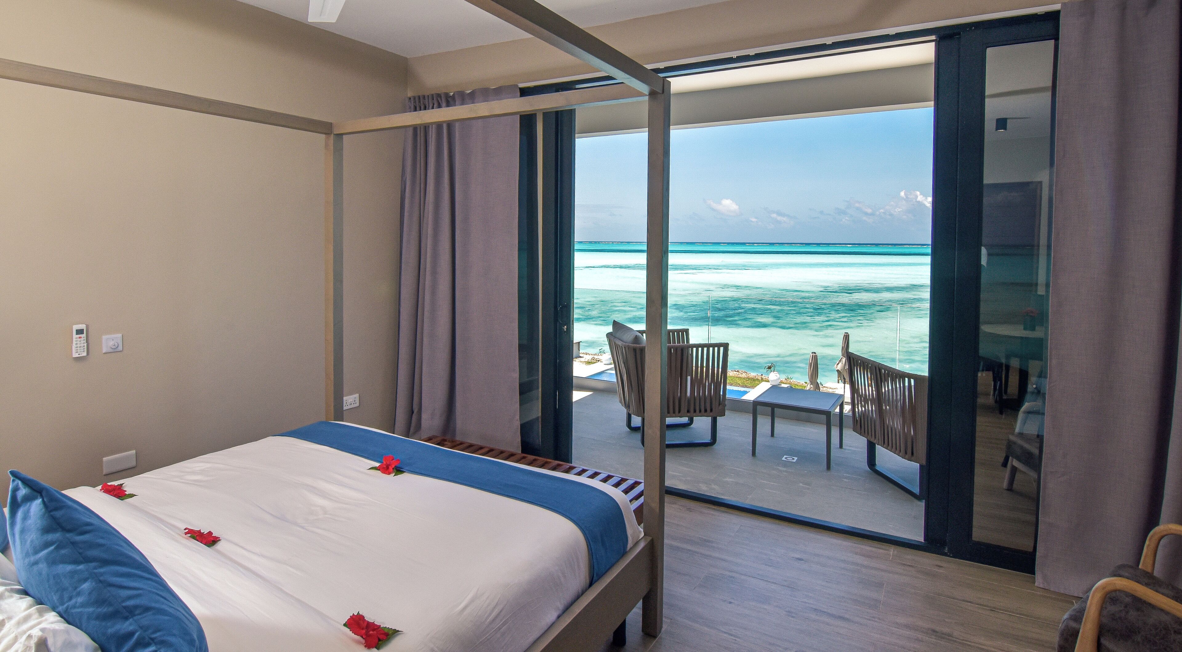 A hotel room with a bed, a small table, and a chair, and a balcony with a view of the ocean.