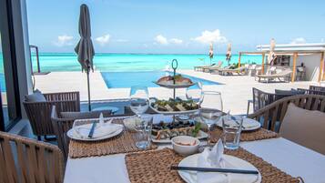 A dining table set with plates, bowls, and glasses, overlooking a pool and the ocean.