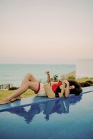 Eine Person liegt auf einer Liege am Pool mit Blick auf den Strand.