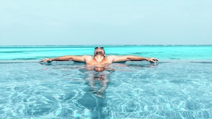 A person floating in a clear blue pool with a view of the ocean and sky. - Villa Bluu (Jambiani)