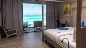 A hotel room with a bed, a desk, a chair, and a view of the ocean. - Villa Bluu (Jambiani)
