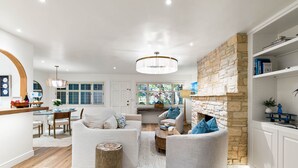 A modern living room with a stone fireplace, white sofas, and a dining area with a wooden table and chairs. - 3972 DolceVita ~Beautiful Remodel, Walk Everywhere (Carmel)