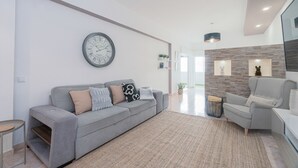A modern living room with a grey sofa, a round wall clock, and a grey armchair. - Central Apartment - Rooftop pool (Albufeira)