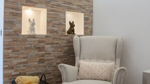 A room with a stone wall, two framed dog sculptures, a grey upholstered armchair with a patterned cushion, and a yellow bag on the floor. - Central Apartment - Rooftop pool (Albufeira)