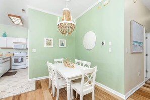 Un comedor con una mesa y sillas blancas, una araña y una cocina al fondo.
