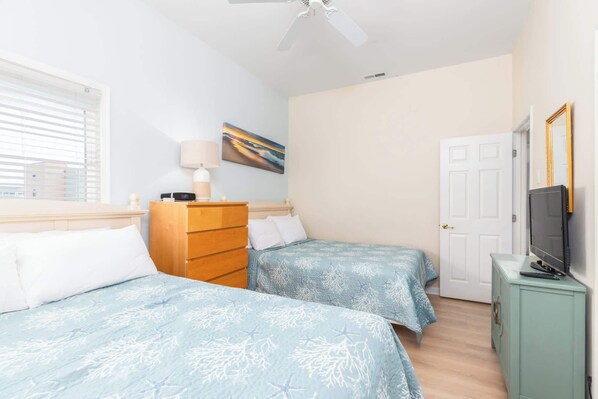 A bedroom with two beds, a dresser, a television on a cabinet, a painting on the wall, and a door.