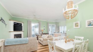 A living room with a fireplace, a dining area with a white table and chairs, and a kitchen in the background. - Waterfront Condo with Pool (Ocean City)